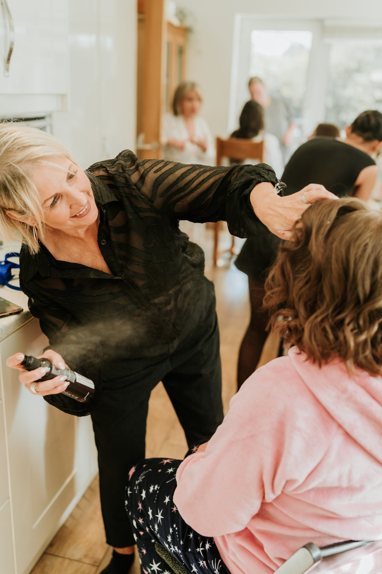 Nikki finishing a bride's hair with hairspray while the bride wears a pink robe.