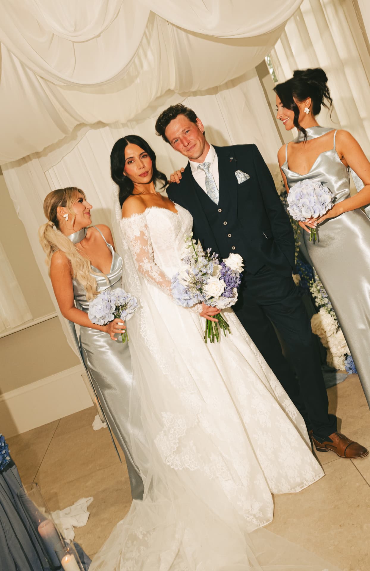 Bride, groom and bridesmaids together beneath white draping.