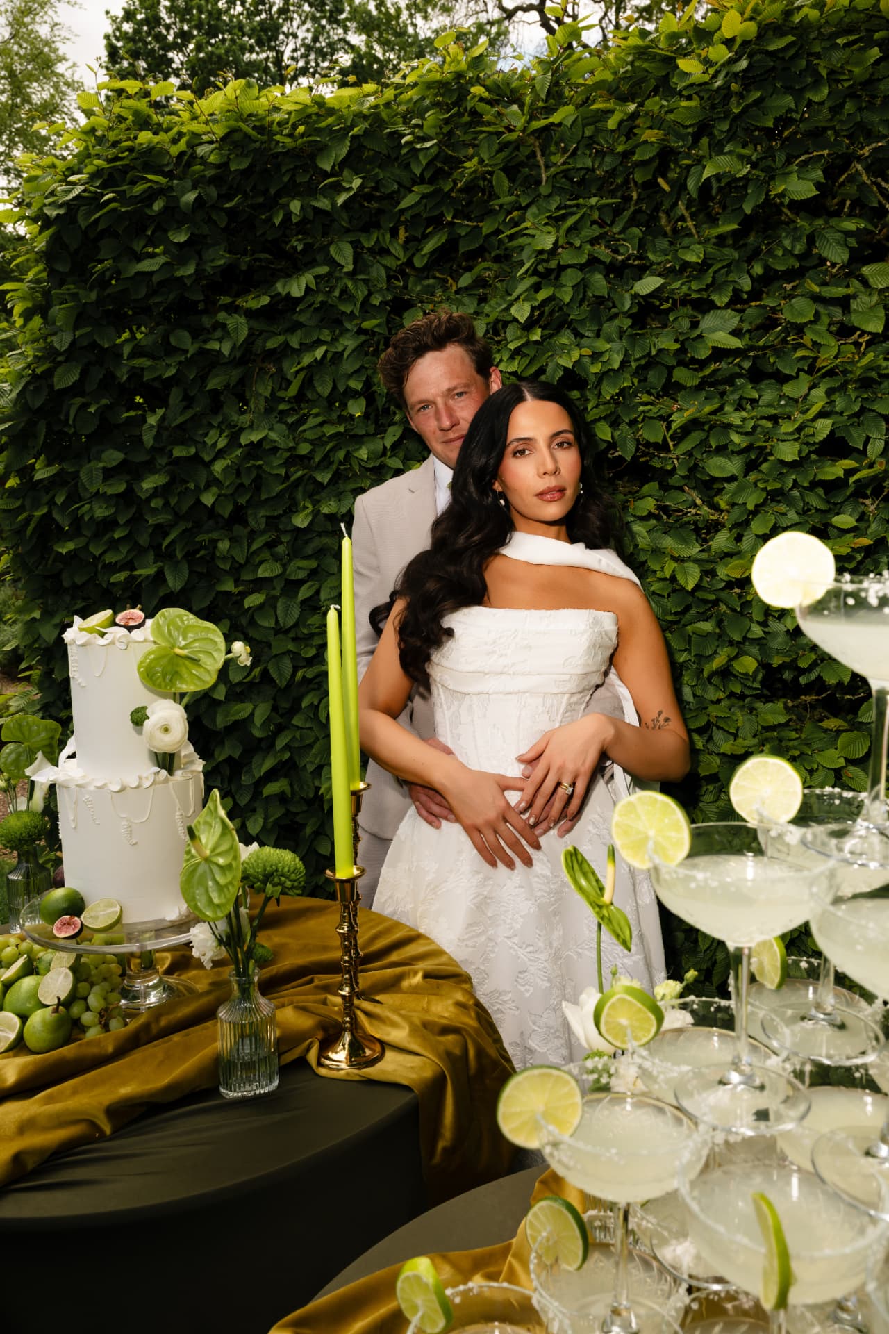 Bride and groom standing behind a cake table beside a tiered margarita tower.