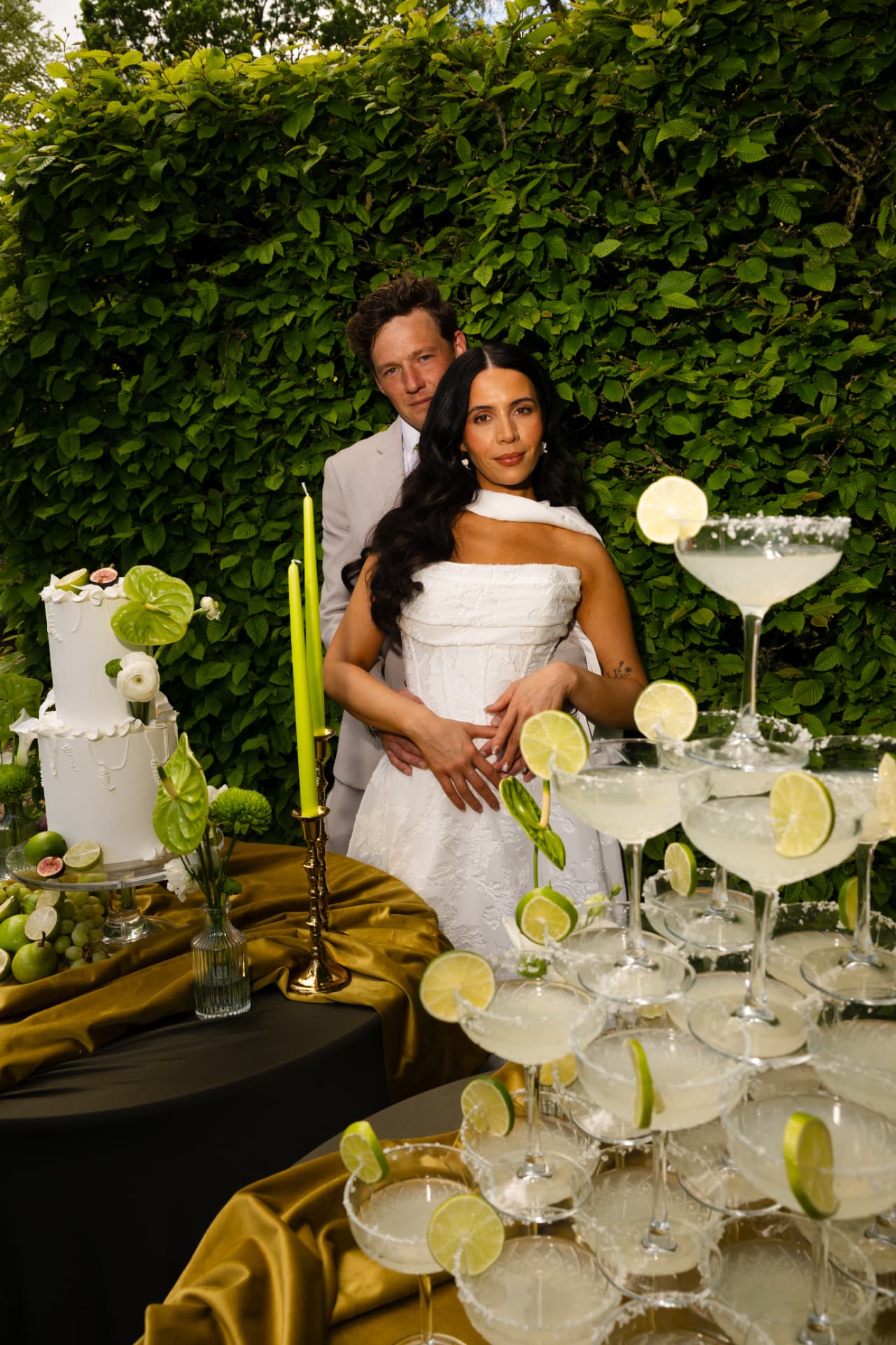 Bride and groom framed by a tiered margarita tower and green foliage.