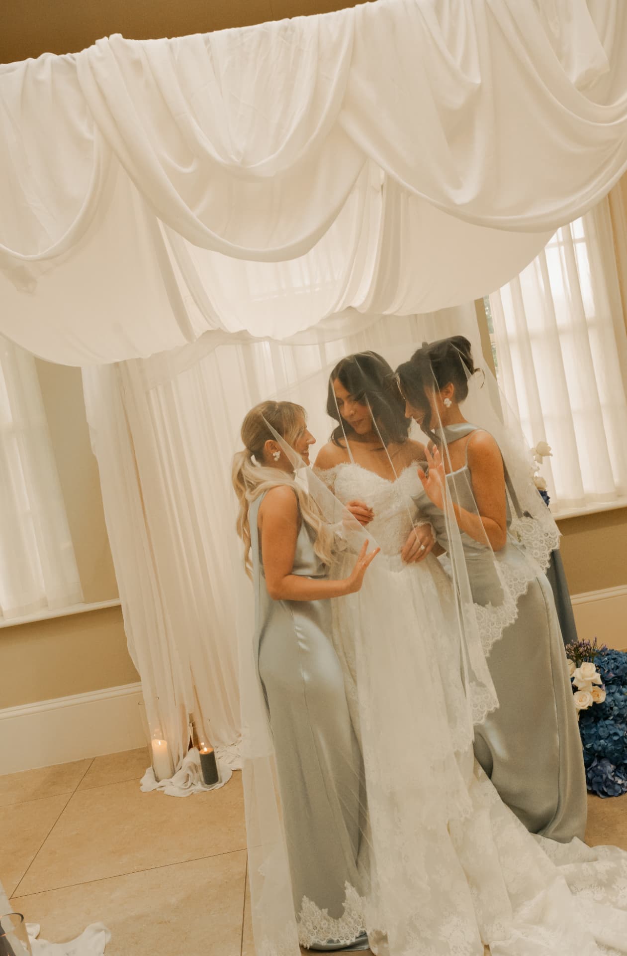 Bride and her bridesmaids gathered together beneath a long veil.