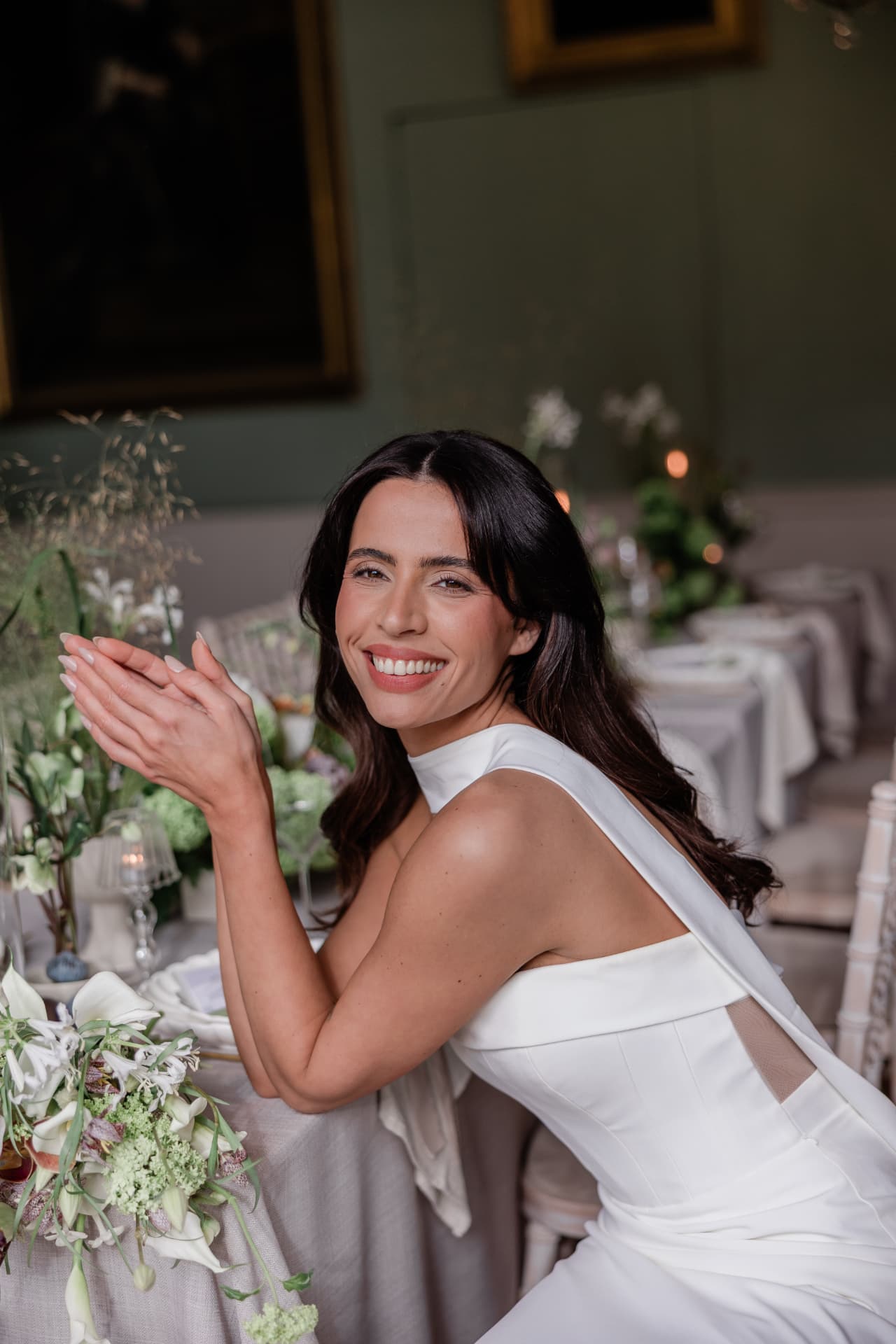 Bride smiling at a dressed dining table beside white spring flowers.