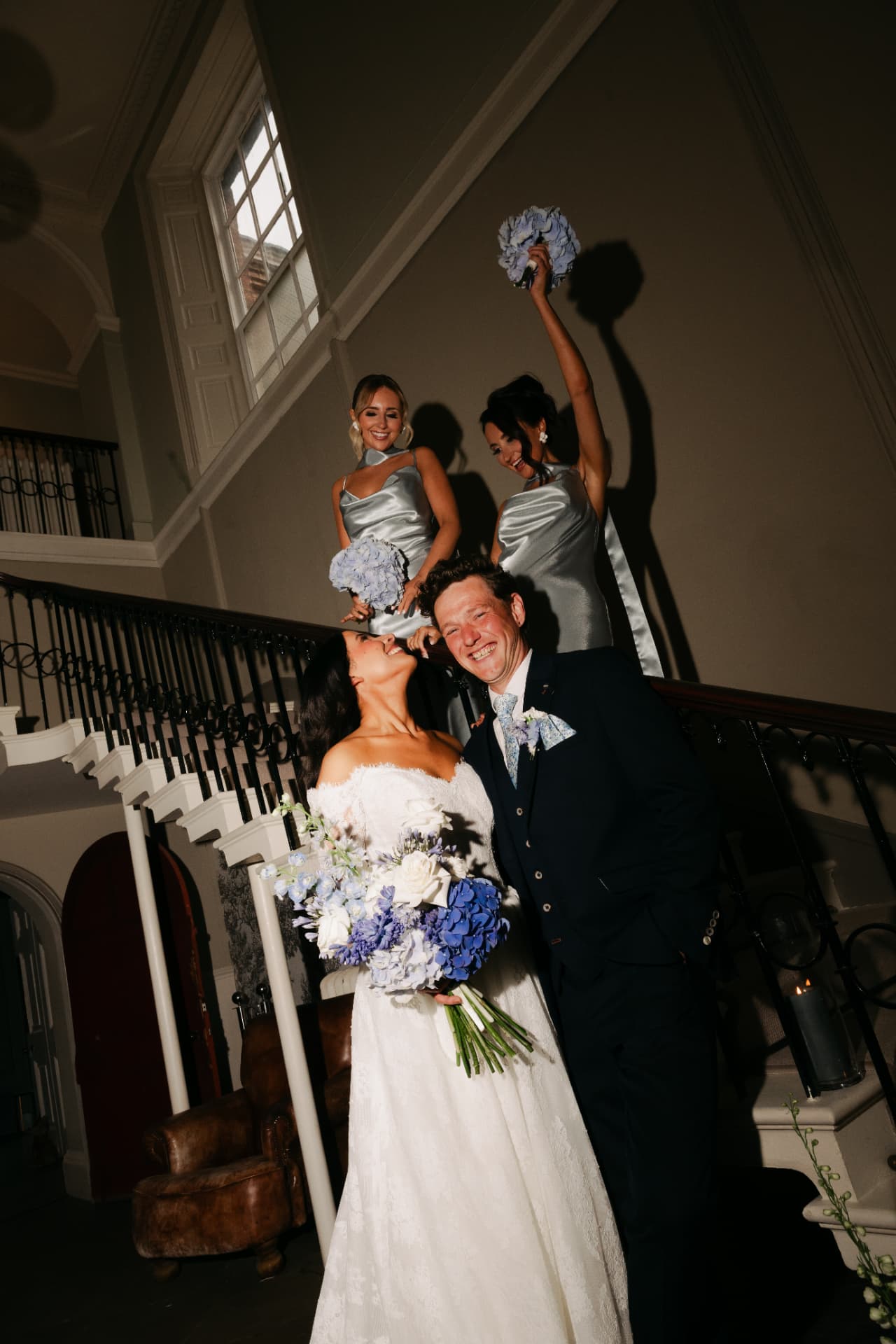 Bride and groom laughing as a bridesmaid raises her bouquet behind them.